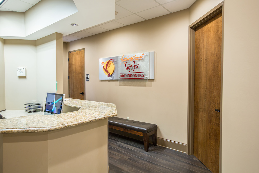 The image shows an interior view of a room with a sign on the wall displaying the name Sweet Tooth Comforts and a counter with a computer monitor, indicating this could be a reception area within a dental or medical office.