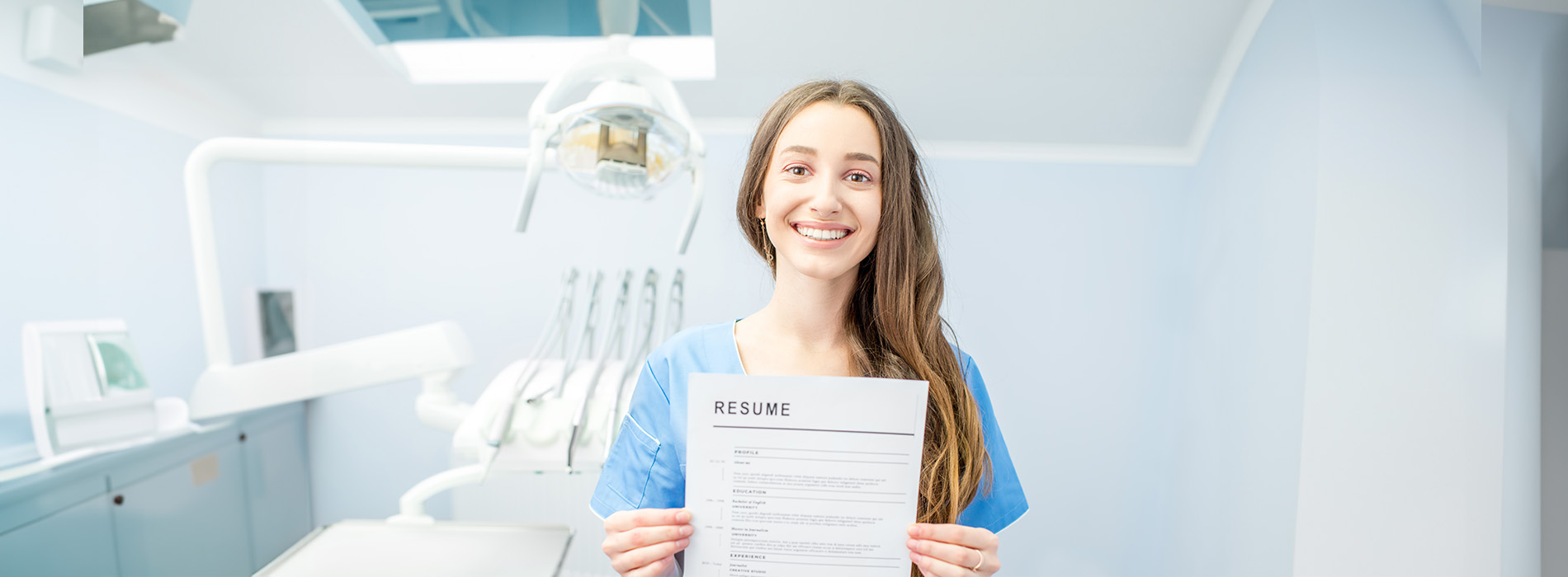 The image features a person standing in front of a dental office with medical equipment, holding a sign, smiling, and wearing a white lab coat.