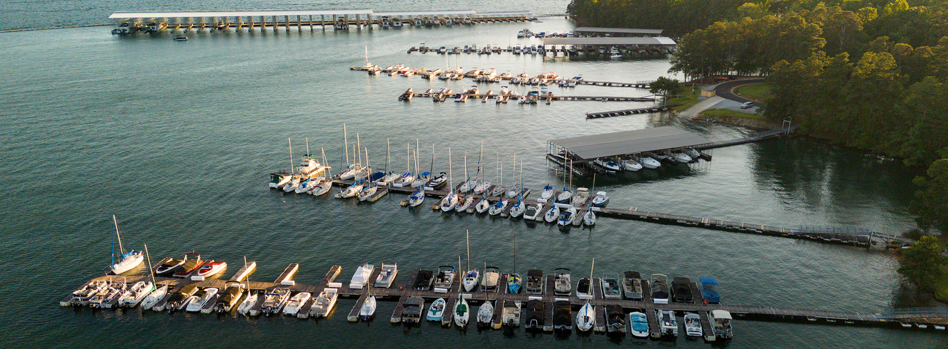 The image shows a marina filled with various boats docked at a pier, with calm water reflecting the boats and a clear sky above.