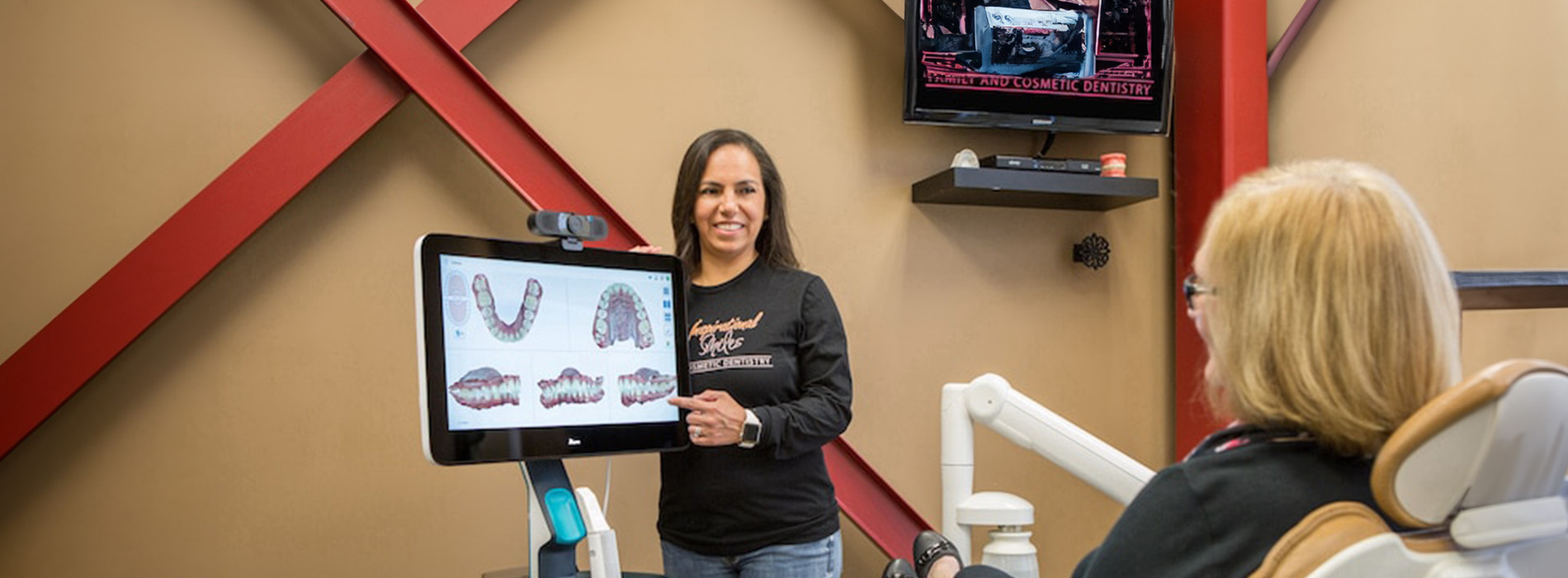 A woman standing behind a dental chair with a tablet displaying images of teeth.