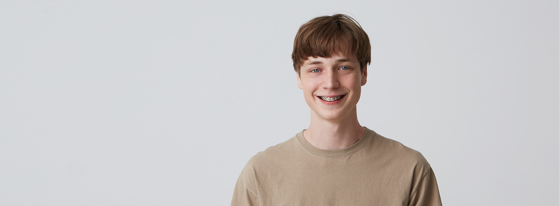 The image shows a young man with short hair smiling at the camera against a plain background.