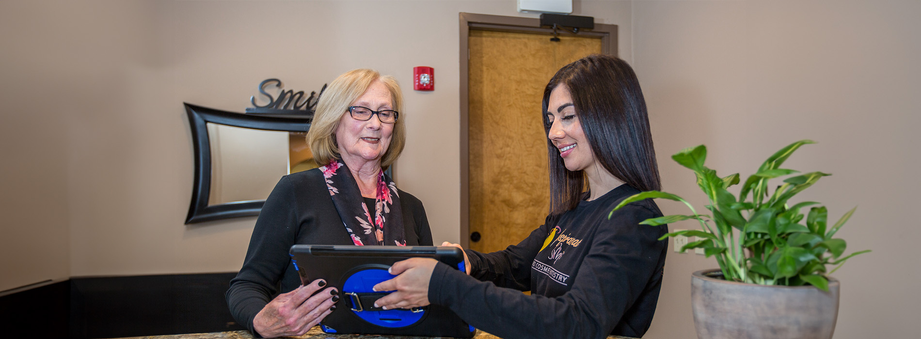 A well-lit reception area with a desk, computer monitor, and potted plant.