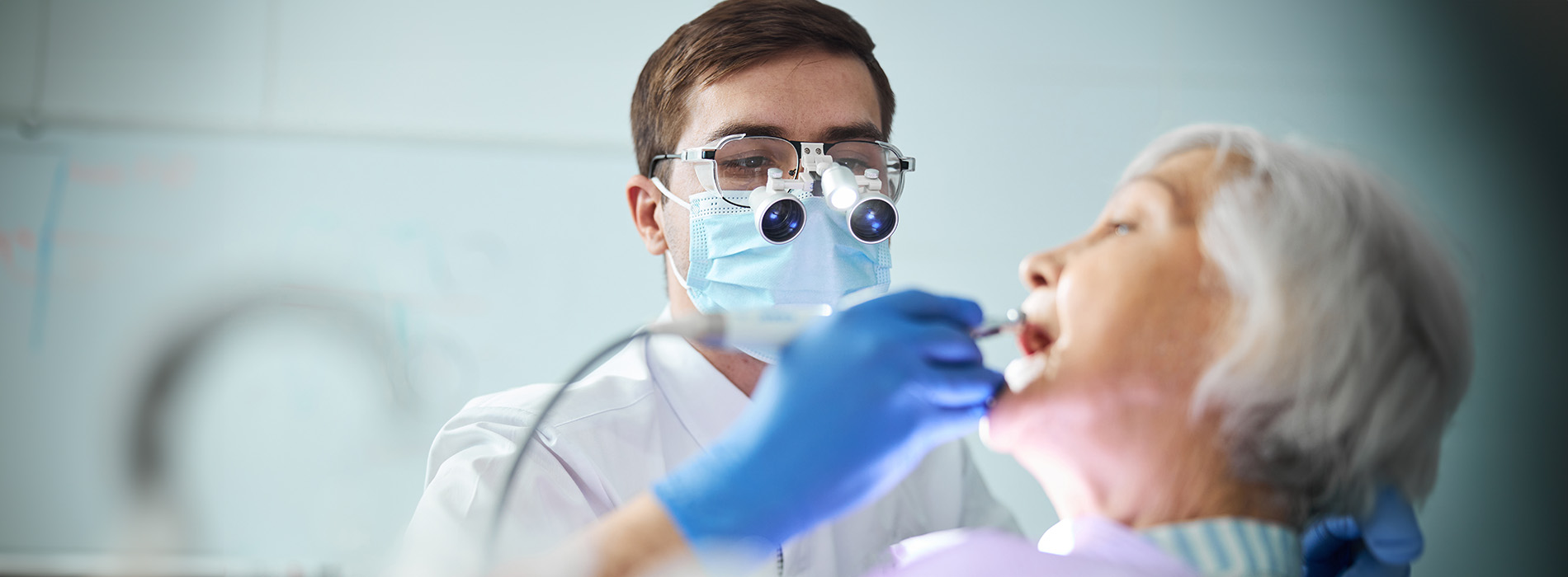 A man and woman in a medical setting the man appears to be assisting with dental care while the woman receives treatment, with medical equipment visible.