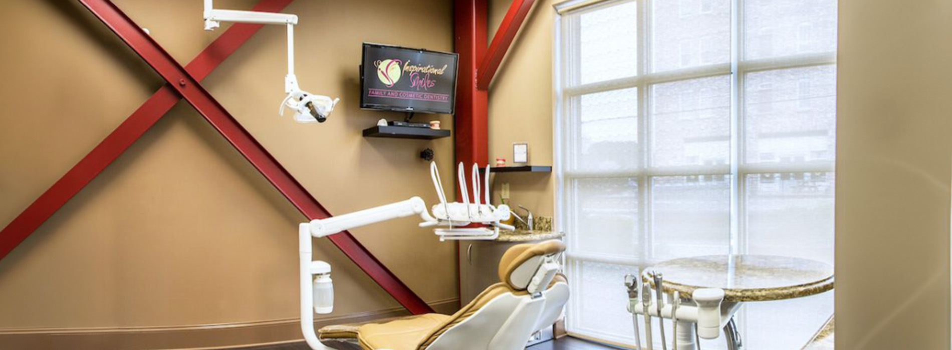 The image shows an interior view of a dental office with modern furnishings and equipment, featuring a reception area with a window and a red beam design on the wall, and a brightly lit treatment room with dental chairs and a large mirror.