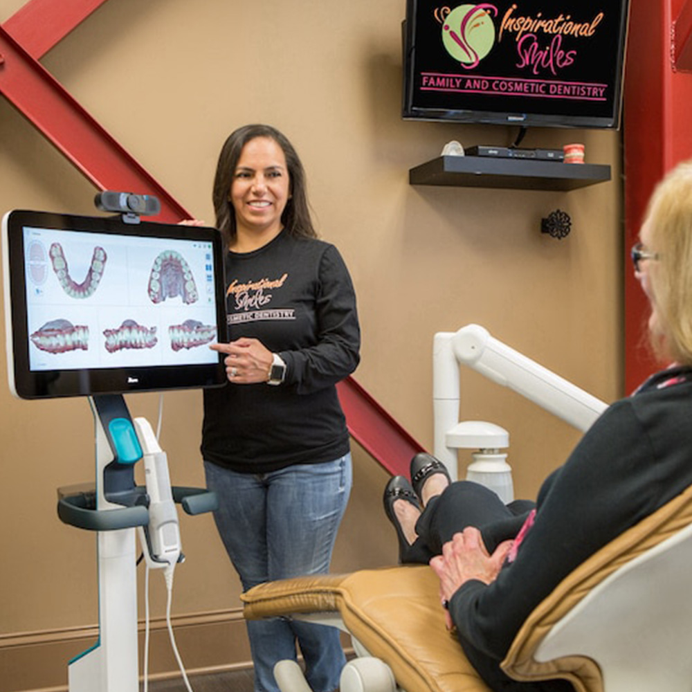 The image shows a woman standing beside a dental chair with a screen displaying a 3D model of a person's teeth, indicating a dental technology demonstration or consultation setting.