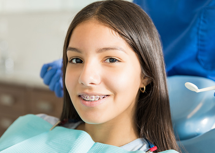 The image shows a young woman sitting in a dental chair, getting her teeth cleaned by a dentist.