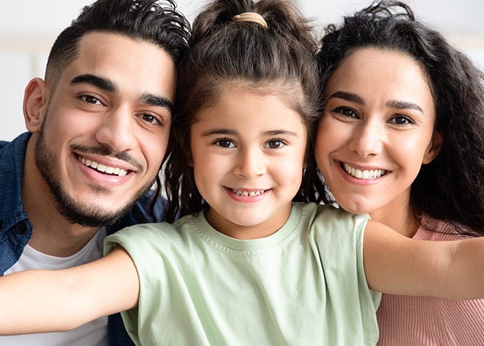 A family of three poses together with smiles, featuring a man, woman, and young child.