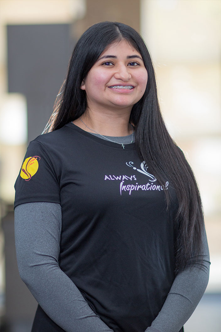 The image shows a person wearing a black t-shirt with white text and a logo, standing in front of a blurred background.