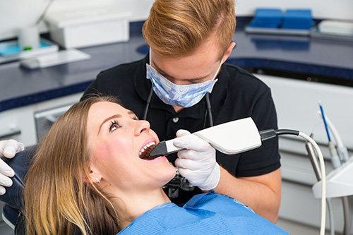 The image shows a dental hygienist performing a teeth cleaning procedure on a patient while wearing personal protective equipment (PPE).