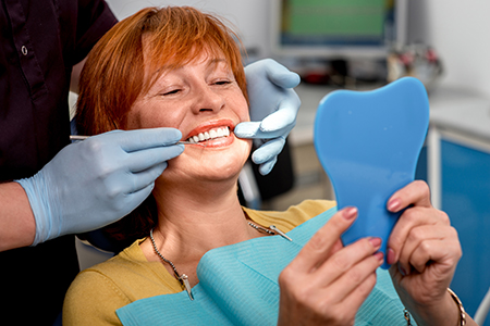 Woman sitting in dental chair with blue dental tray, holding toothbrush, smiling at camera.