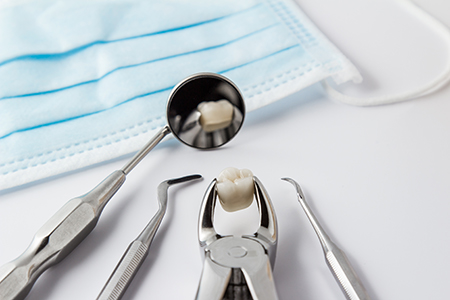 This image shows a dental hygiene setting with various dental tools including a drill, a mirror, and a toothbrush, along with a tray of dental instruments and a blue surgical mask on a table.