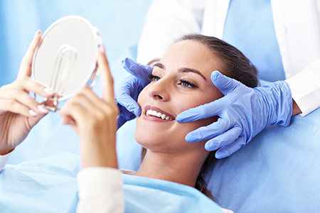 The image shows a woman sitting in a dental chair with a mirror held up to her face, a dentist standing behind her holding a magnifying glass over her eyes, and another person taking a photo of the scene.