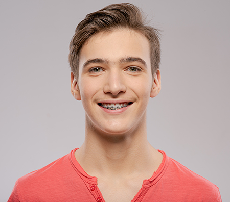The image shows a young man with a bright smile, wearing a red shirt, against a white background.