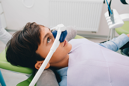A young person lying down with an open mouth, wearing a dental device over their face, likely at a dentist's office.