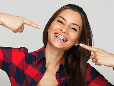A woman with a wide smile, pointing to her teeth, against a white background.